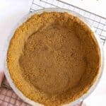 Graham cracker pie crust in a pan on a cooling rack.