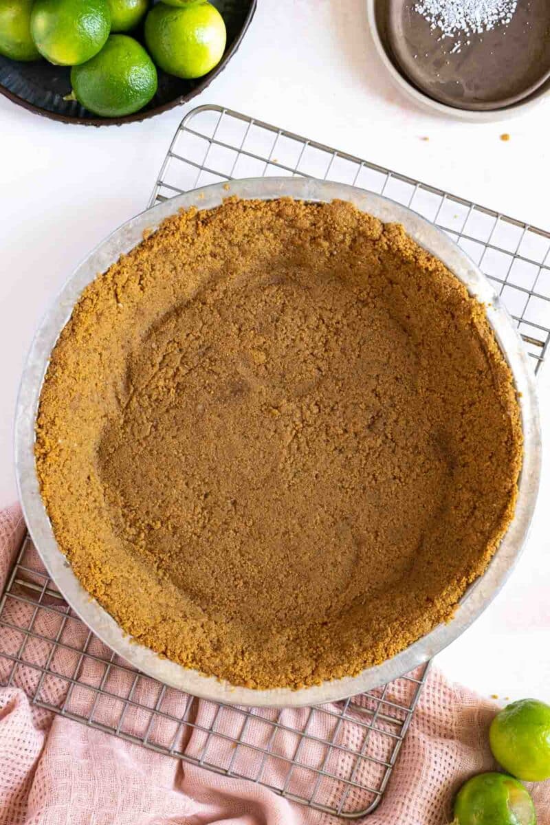 Graham cracker pie crust in a pan on a cooling rack.