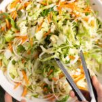 Mixing coleslaw in a bowl with tongs.