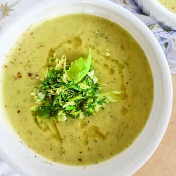 Soup in a white bowl with celery leaves.