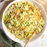 Coleslaw in a white bowl with a wooden spoon.