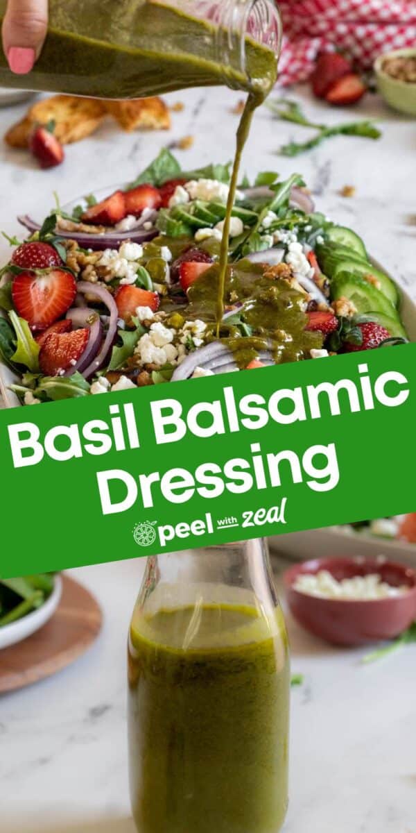 A green basil balsamic vinaigrette is being poured onto a fresh salad with strawberries, onions, cucumber, and feta, with a bottle of dressing in the foreground.
