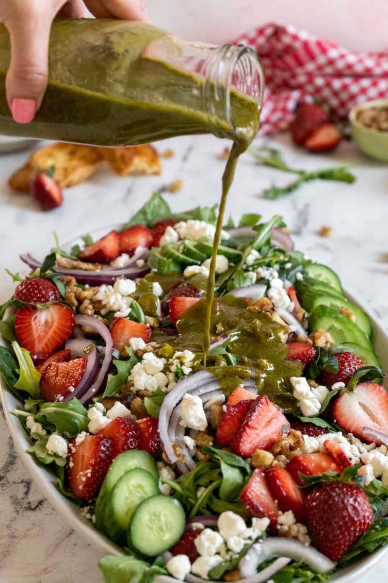 Pouring basil balsamic dressing on a salad.