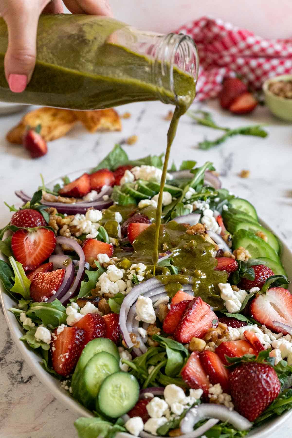 Pouring basil balsamic dressing on a salad.