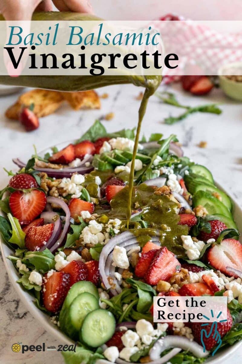 Basil balsamic vinaigrette is drizzled over a fresh salad of strawberries, cucumbers, red onions, walnuts, and feta cheese on a platter.
