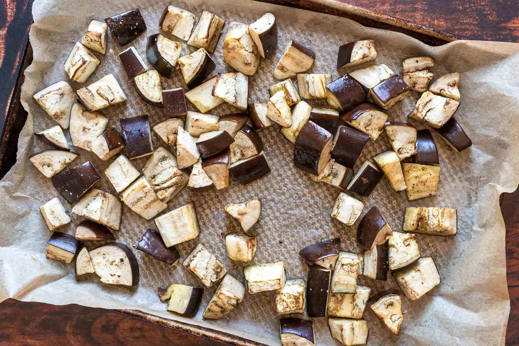 Cubed pieces of eggplant, perfect for making eggplant caponata, are spread out on a parchment-lined baking sheet, ready for roasting.