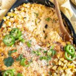 Elote dip in a pan with a wooden spoon.