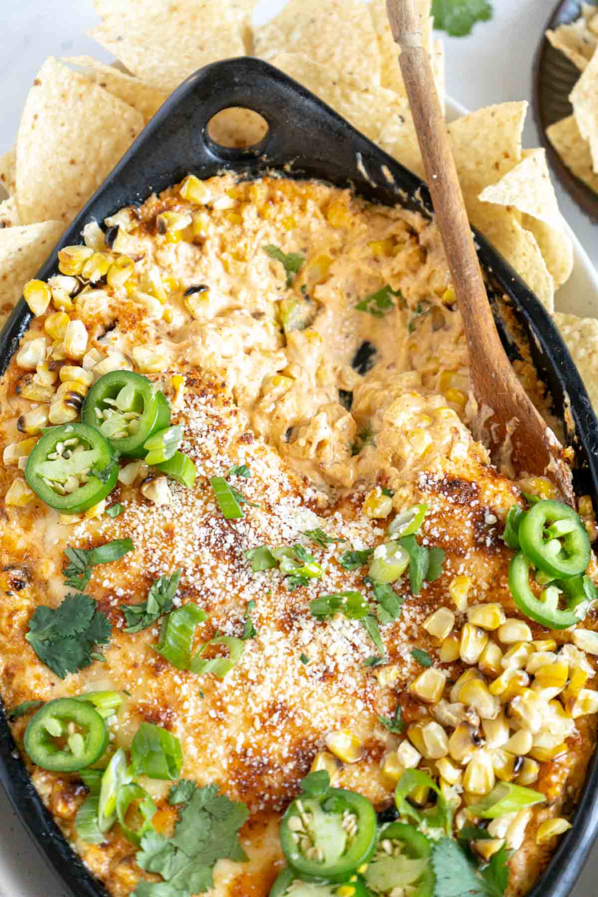 Elote dip in a pan with a wooden spoon.