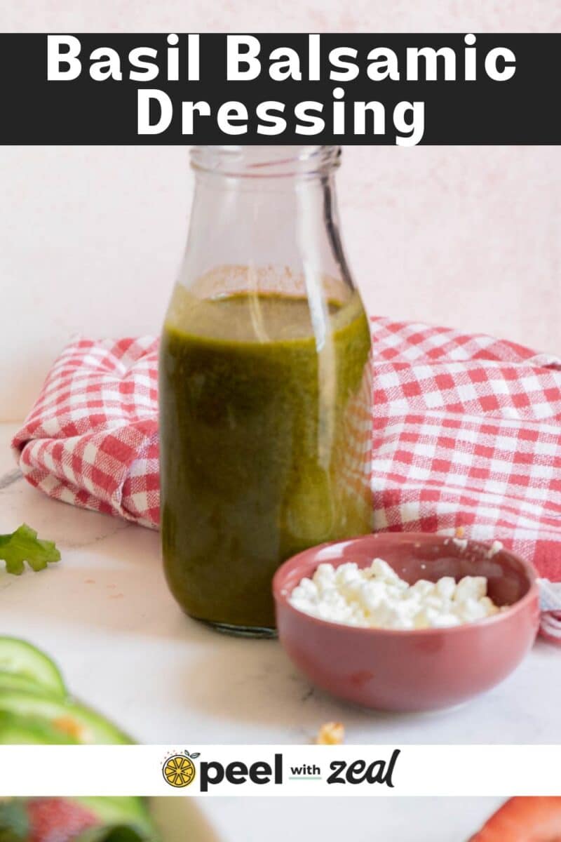 A glass bottle of basil balsamic vinaigrette sits on a counter next to a small bowl of cottage cheese and a red checkered cloth.