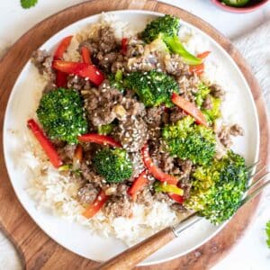 Ground beef and broccoli serve over rice on a white plate.