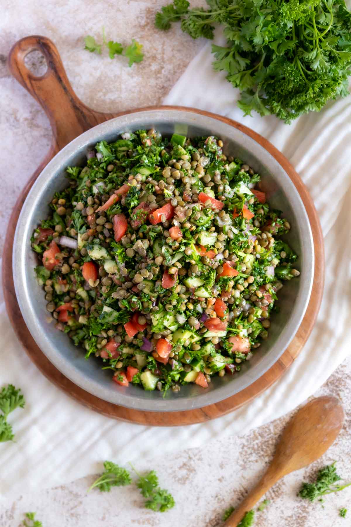 Tabbouleh in a serving dish with a wooden spoon and parsley leaves.