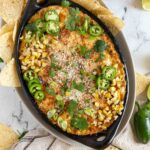 Mexican corn dip in a pan with tortilla chips, jalapenos, and cilantro.