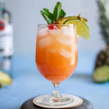 Rum punch cocktail in a glass with a pineapple wedge and mint.