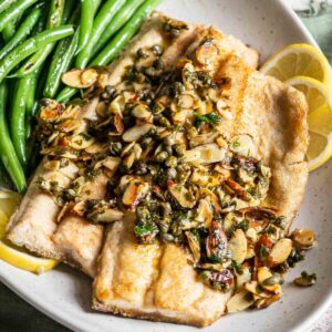 Trout with butter sauce and almonds on a plate with green beans.