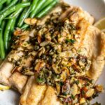 Trout with butter sauce and almonds on a plate with green beans.