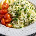 Zucchini risotto in a white bowl with cherry tomatoes.