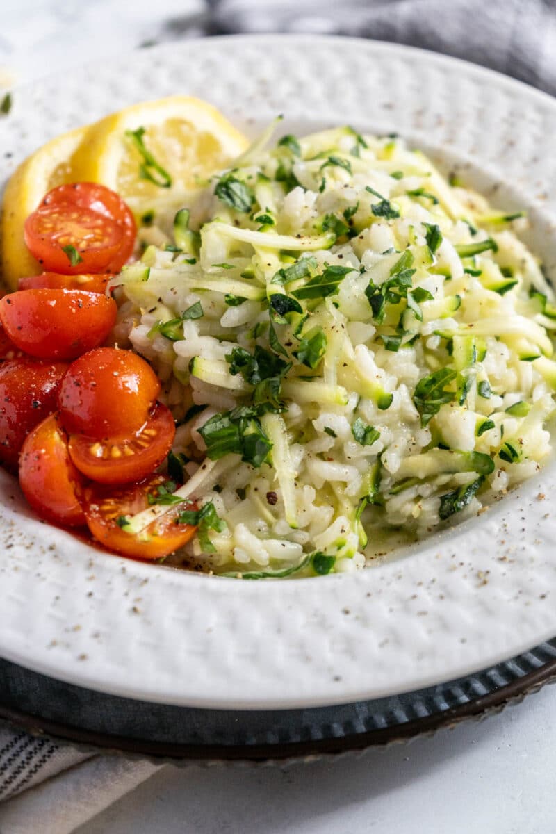Zucchini risotto in a white bowl with cherry tomatoes.