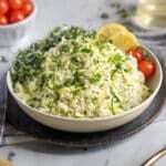 Risotto in a bowl with grated zucchini, microgreens, lemon slices and tomatoes.