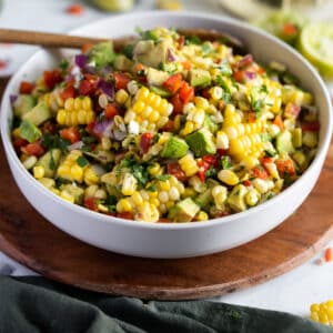 Bowl with avocado and corn salad on a cutting board with a wooden spoon.