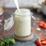 Creamy poppy seed dressing in a bottle with strawberries.