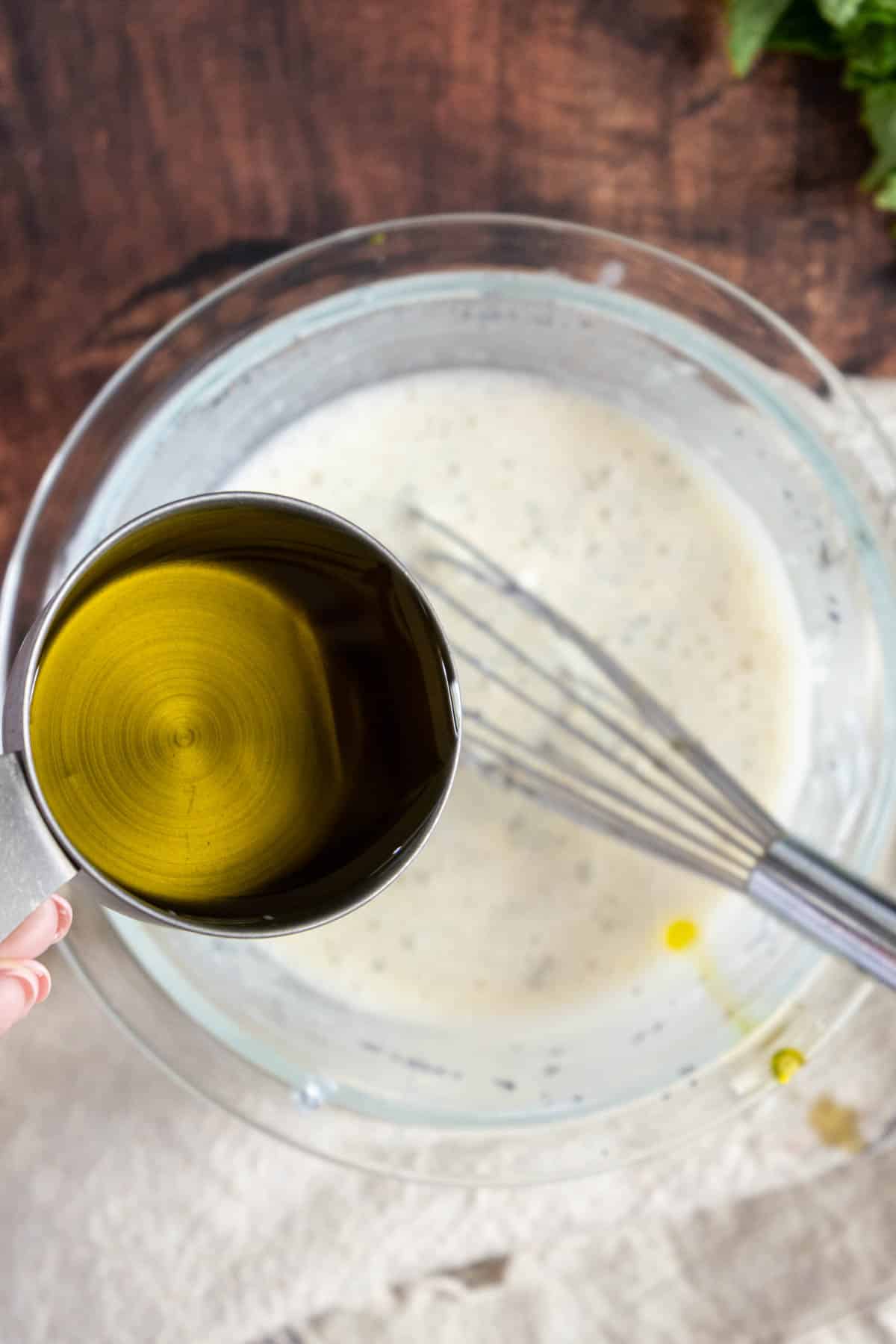 Drizzling olive oil into salad dressing.