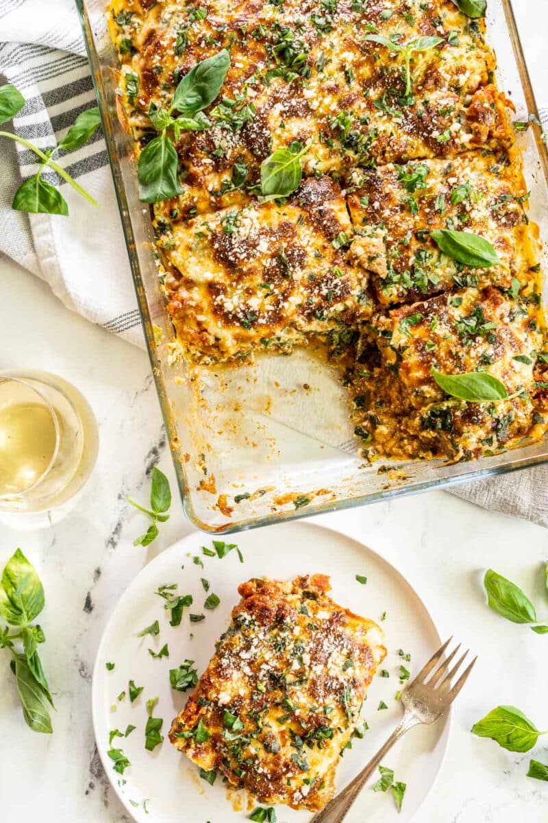 Slice of lasagna on a plate next to a casserole dish.