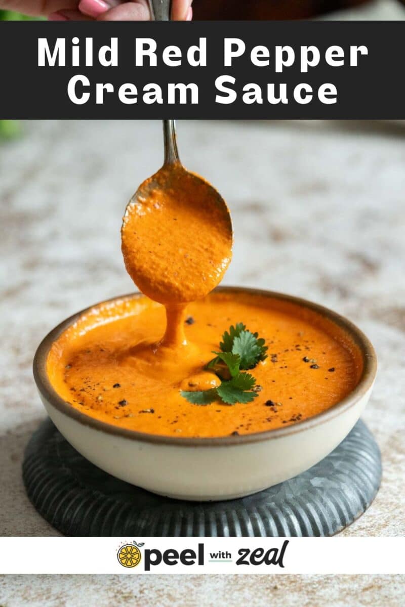 A spoon drizzles red pepper crema into a bowl, garnished with cilantro and black pepper. The text "Mild Red Pepper Cream Sauce" is visible at the top.