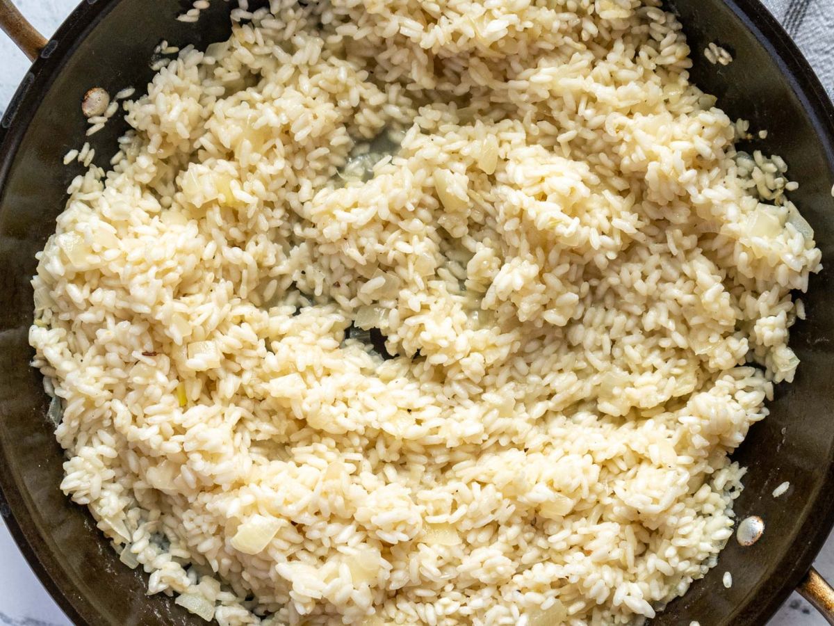 A close-up view of a pan filled with creamy zucchini risotto, showing soft rice grains, tender zucchini pieces, and small bits of onion in a thick, pale sauce.