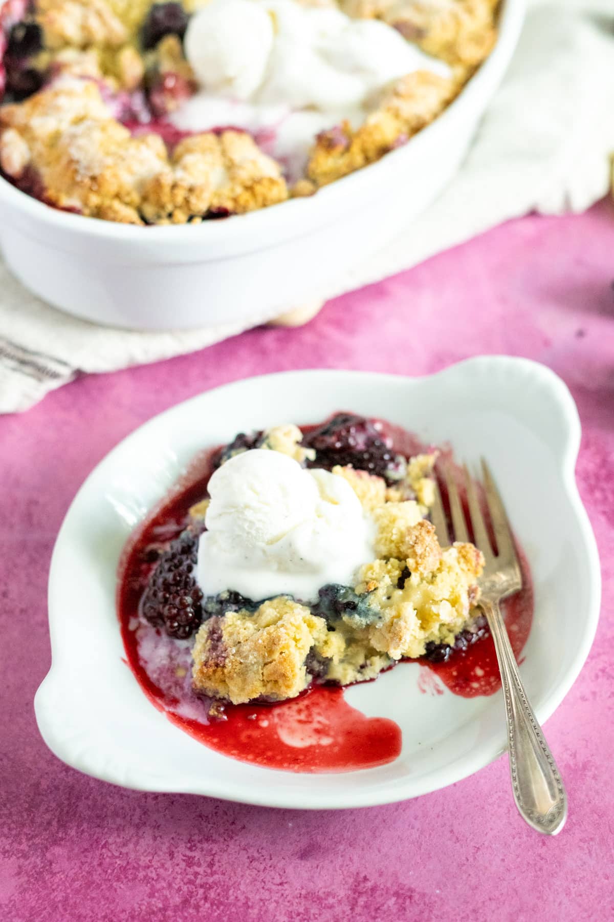 Serving of gluten free cobbler on a plate with a scoop of ice cream and a fork.