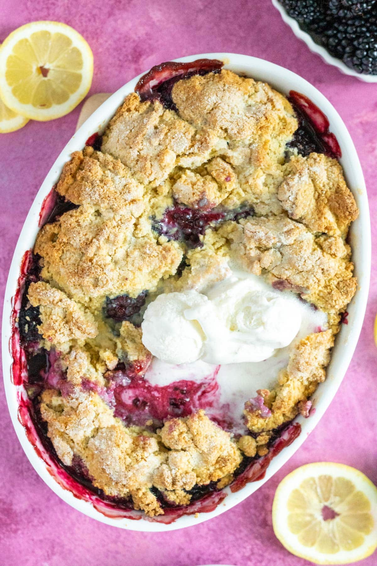 Gluten free berry cobbler in a baking dish with lemon slices and a bowl of berries.