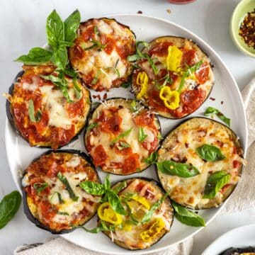 Mini Eggplant pizzas on a plate with different pizza toppings and fresh basil.