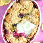 Blackberry cobbler in a baking dish with ice cream and lemon slices.