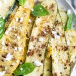 Grilled zucchini and squash on a plate with fresh basil leaves and cheese.