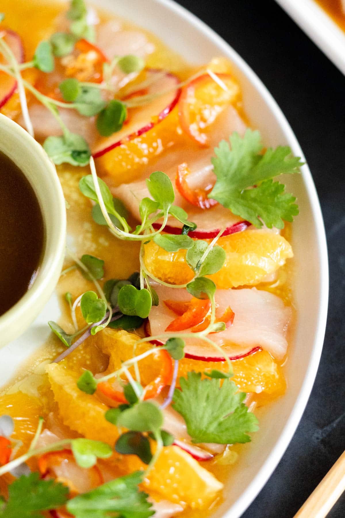 Hamachi crudo with orange slices, soy dipping sauce, and cilantro.