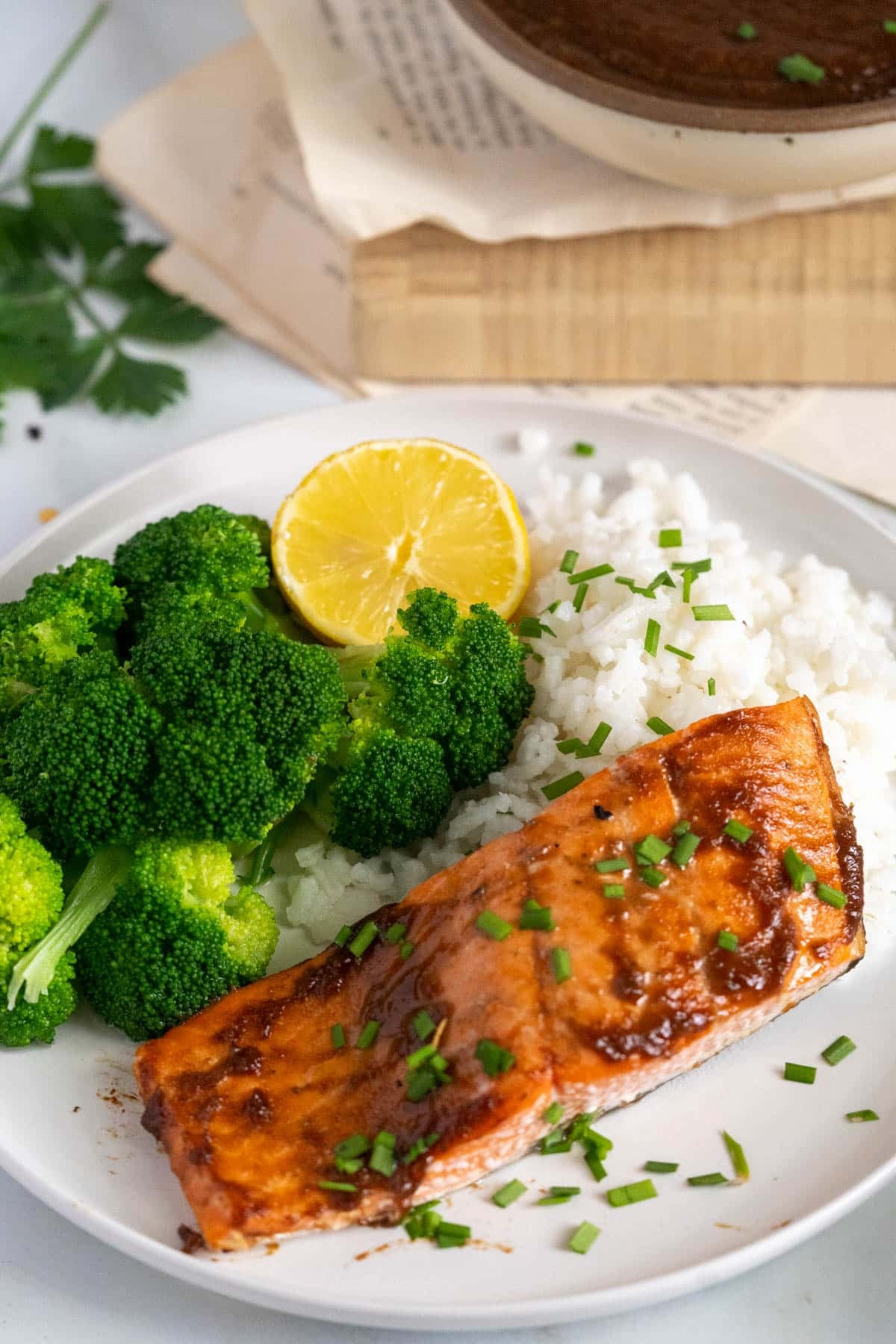 A plate with a grilled salmon fillet, steamed broccoli, white rice, a lemon slice, and chopped chives on top.