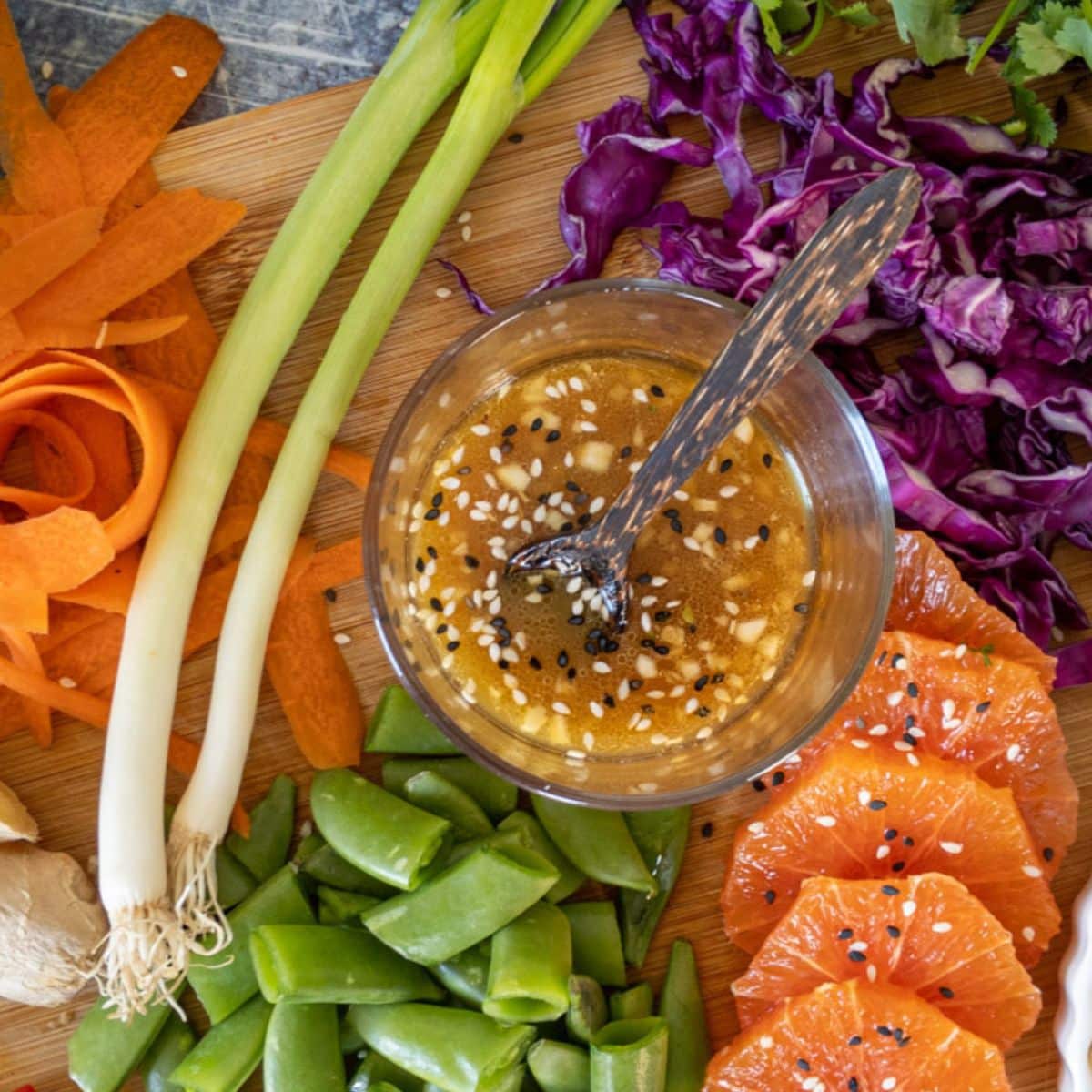 Dressing in a bowl with sesame seeds, vegetables, and sliced oranges.