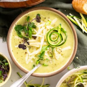 Bowl of zucchini soup with fresh herbs and grated cheese.