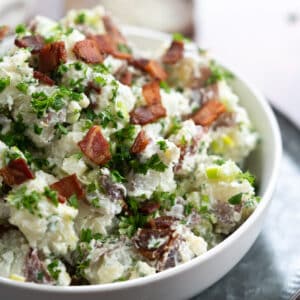 Potato salad in a bowl with blue cheese, bacon and fresh herbs.