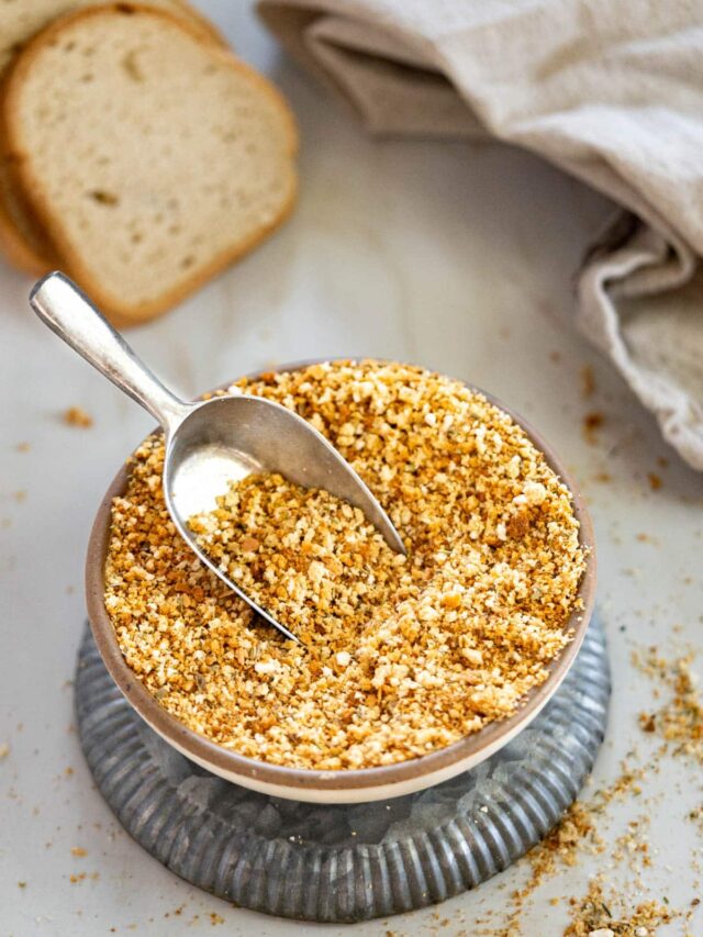 Gluten-free bread crumbs in a bowl with a loaf of GF bread in the back.