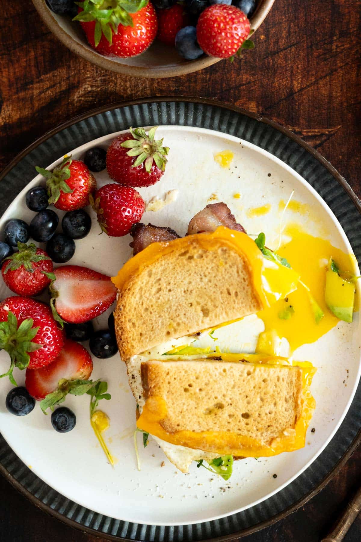 A runny egg sandwich on a plate with fresh fruit.