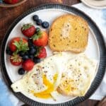 A breakfast plate with over easy eggs, toast and fresh berries.