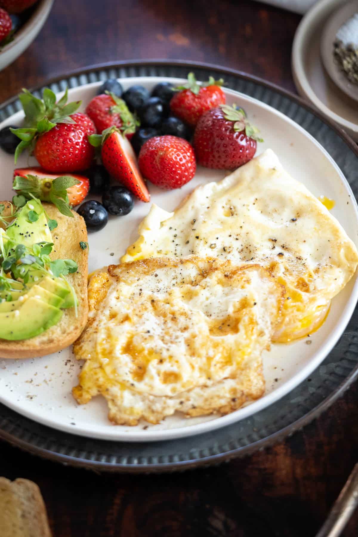 Fried egg with firm yolks on a plate with fruit and avocado toast.