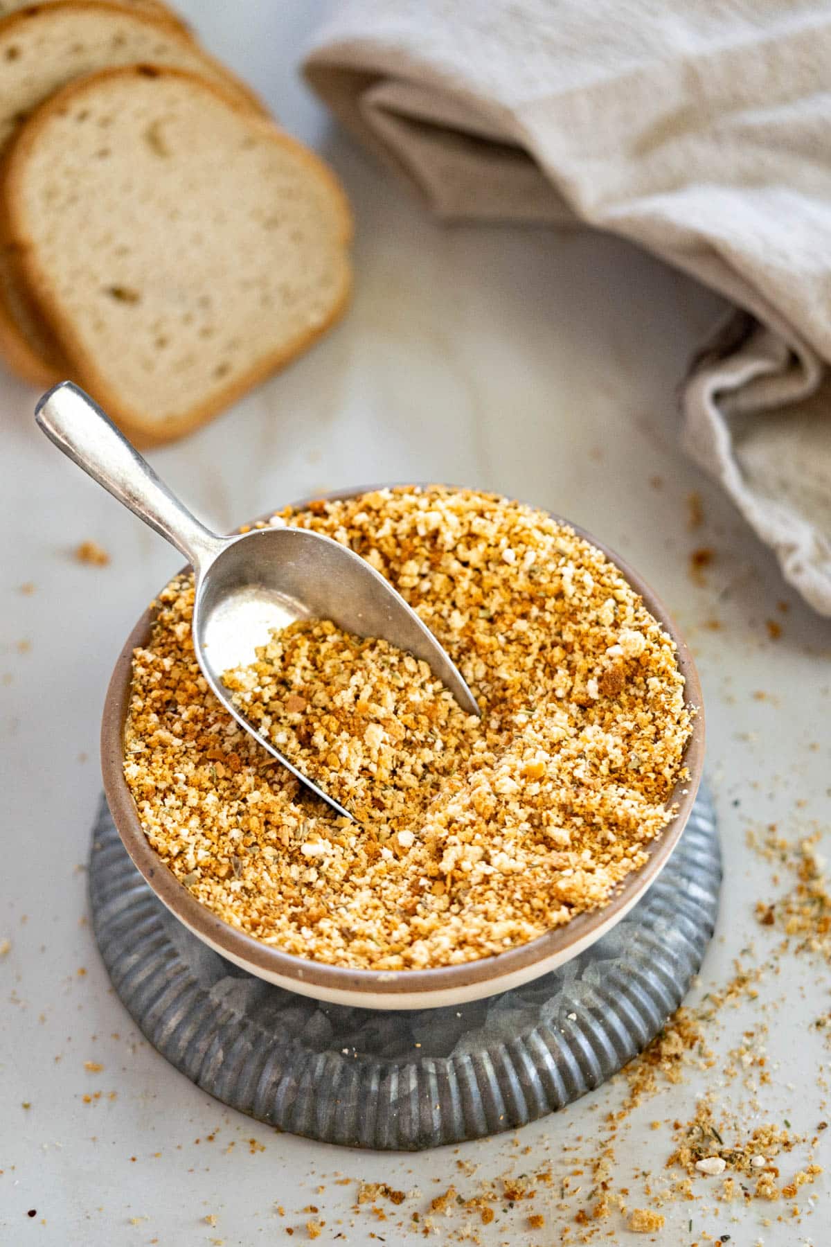 Gluten-free bread crumbs in a bowl with a loaf of GF bread in the back.