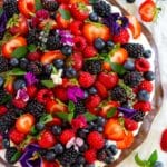 Gluten free dessert pizza with cream cheese frosting and fresh fruit and mint leaves.