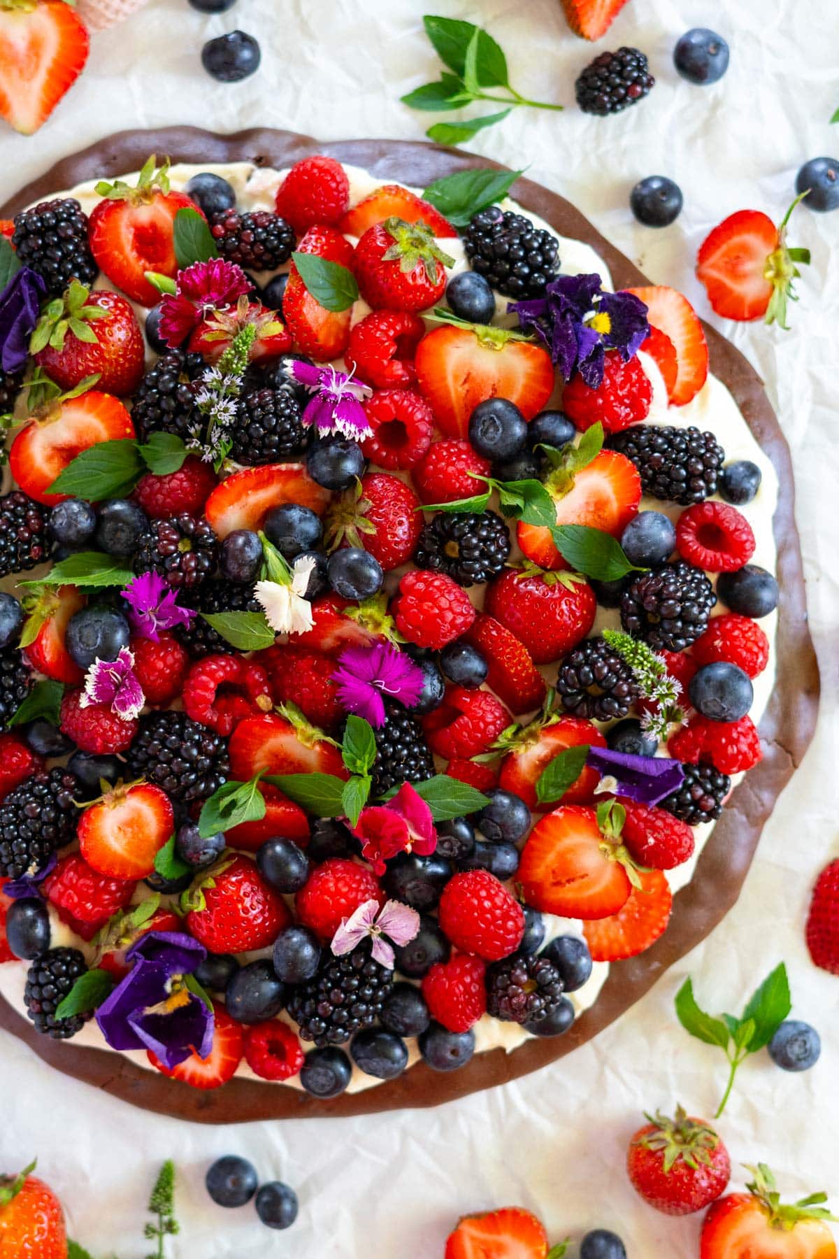 Gluten free dessert pizza with cream cheese frosting and fresh fruit and mint leaves.