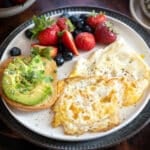 Eggs over hard on a plate with fresh berries and avocado toast.