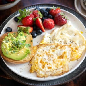 Eggs over hard on a plate with fresh berries and avocado toast.