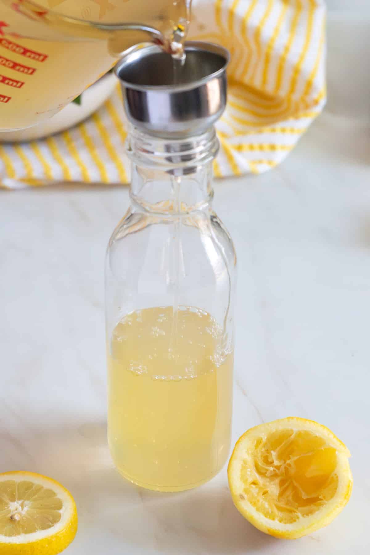 Pouring simple syrup into a bottle with cut lemons on a counter.