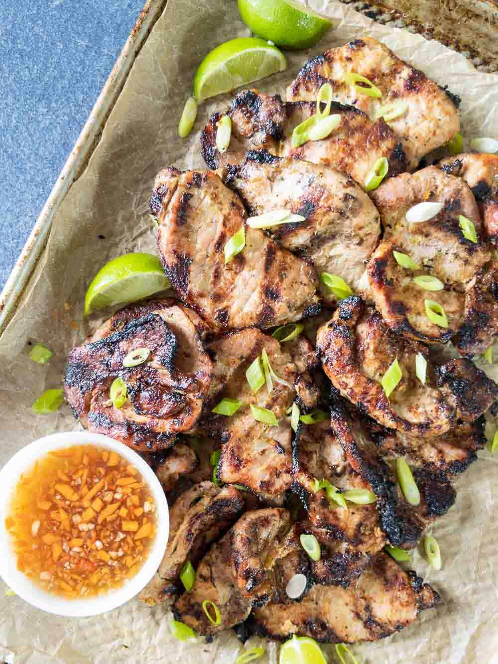 Grilled Vietnamese pork on a serving platter with dipping sauce and fresh lime slices.