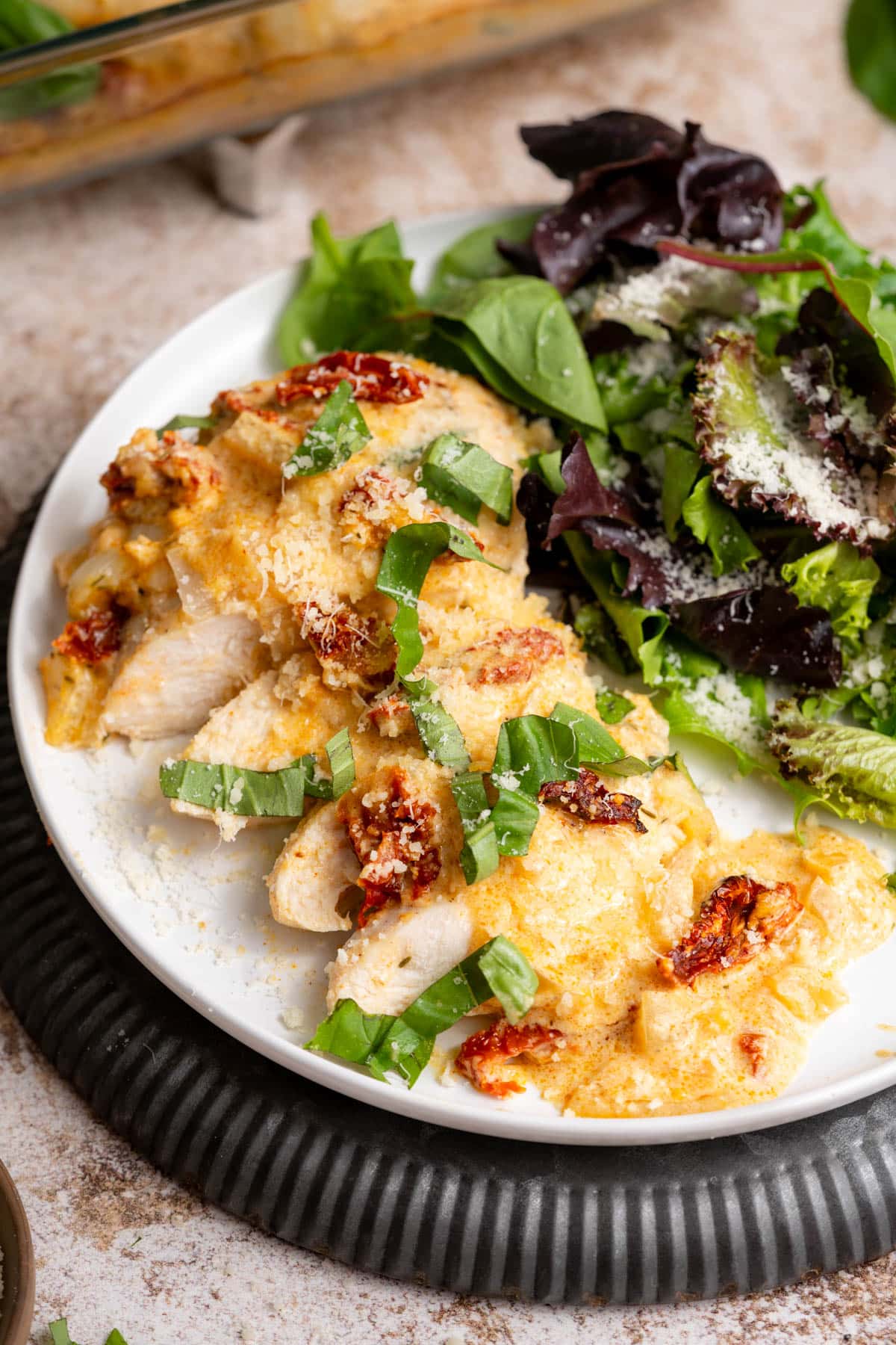 Sliced tuscan chicken on a plate with a green salad.